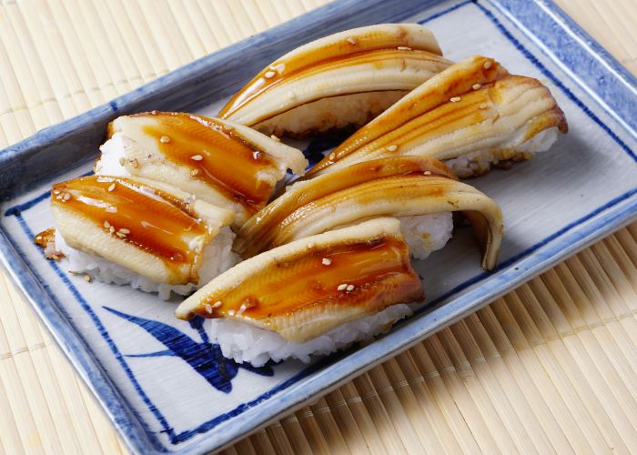 Anago eel nigiri, served on a blue and white porcelain serving tray and covered in sauce.